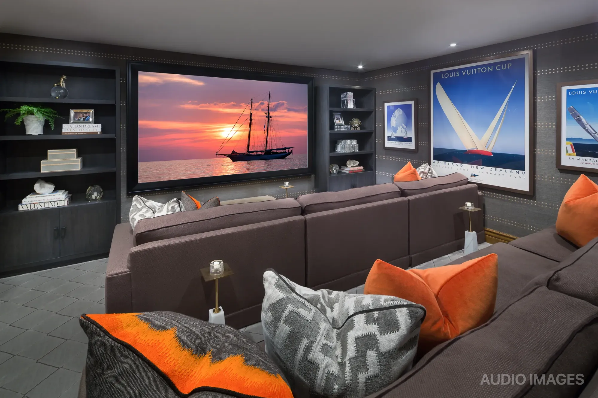 The downstairs media room, its screen showing a sailboat at sunset between built-in shelving.