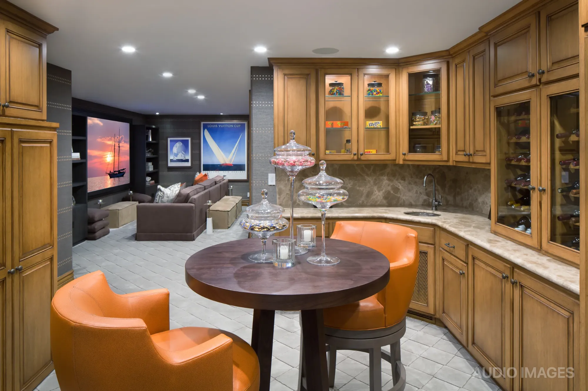 The media room bar with wooden cabinetry, orange barstools, and the projection screen alongside.