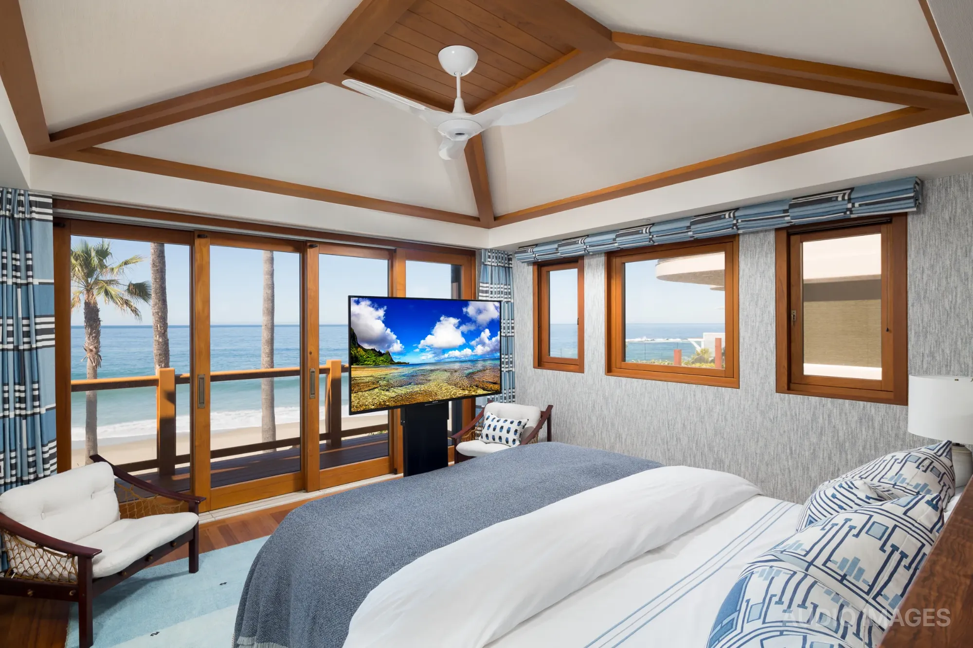 An oceanfront primary bedroom with a retractable television rising in front of floor-to-ceiling glass doors that open to the Pacific.