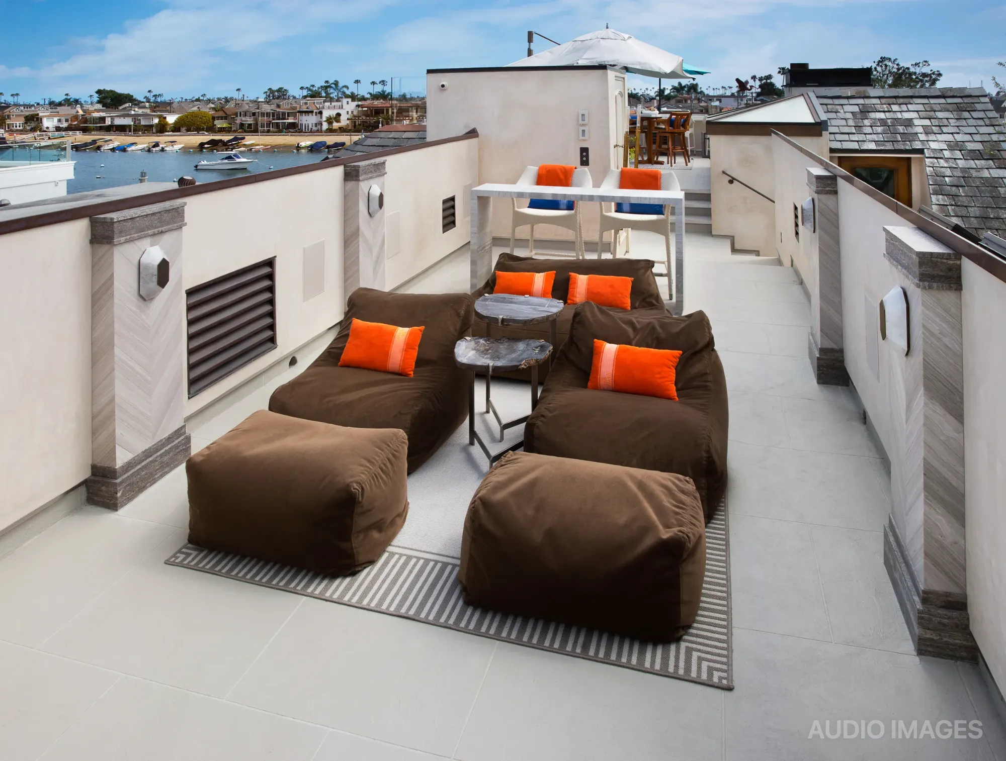 The full rooftop deck — lounge seating, striped rug, and dining area overlooking the harbor.