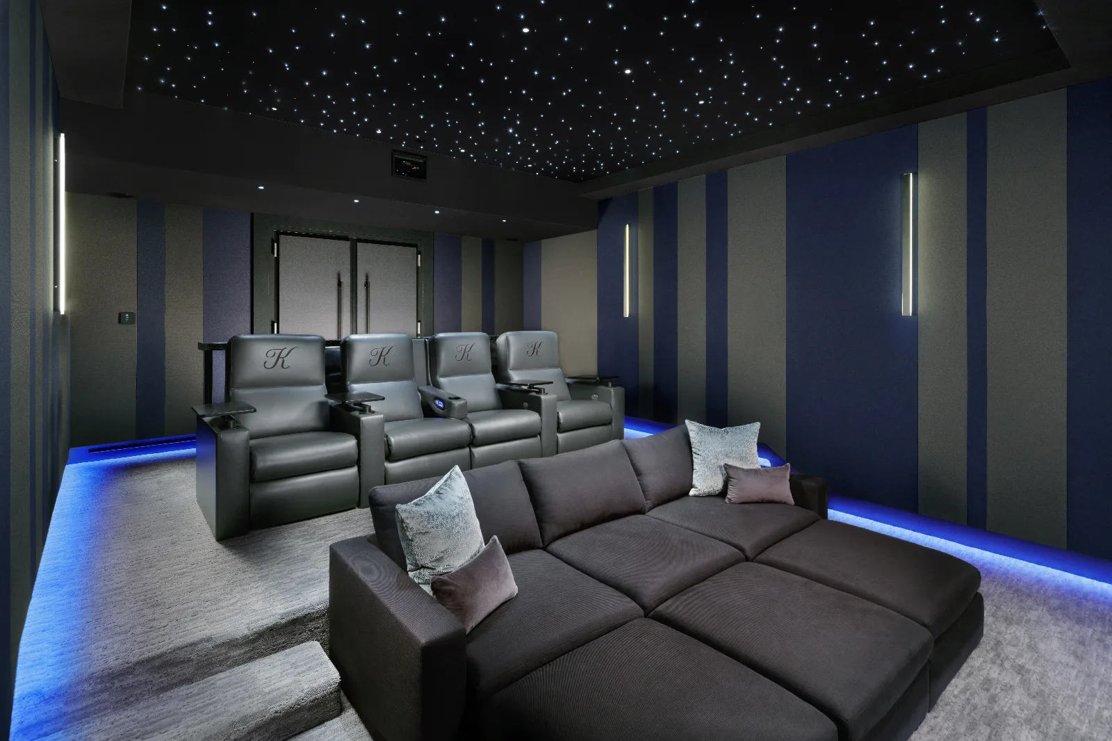 Modern home theater with a dark starry ceiling, blue accent lighting, a large sectional, and four recliner seats.