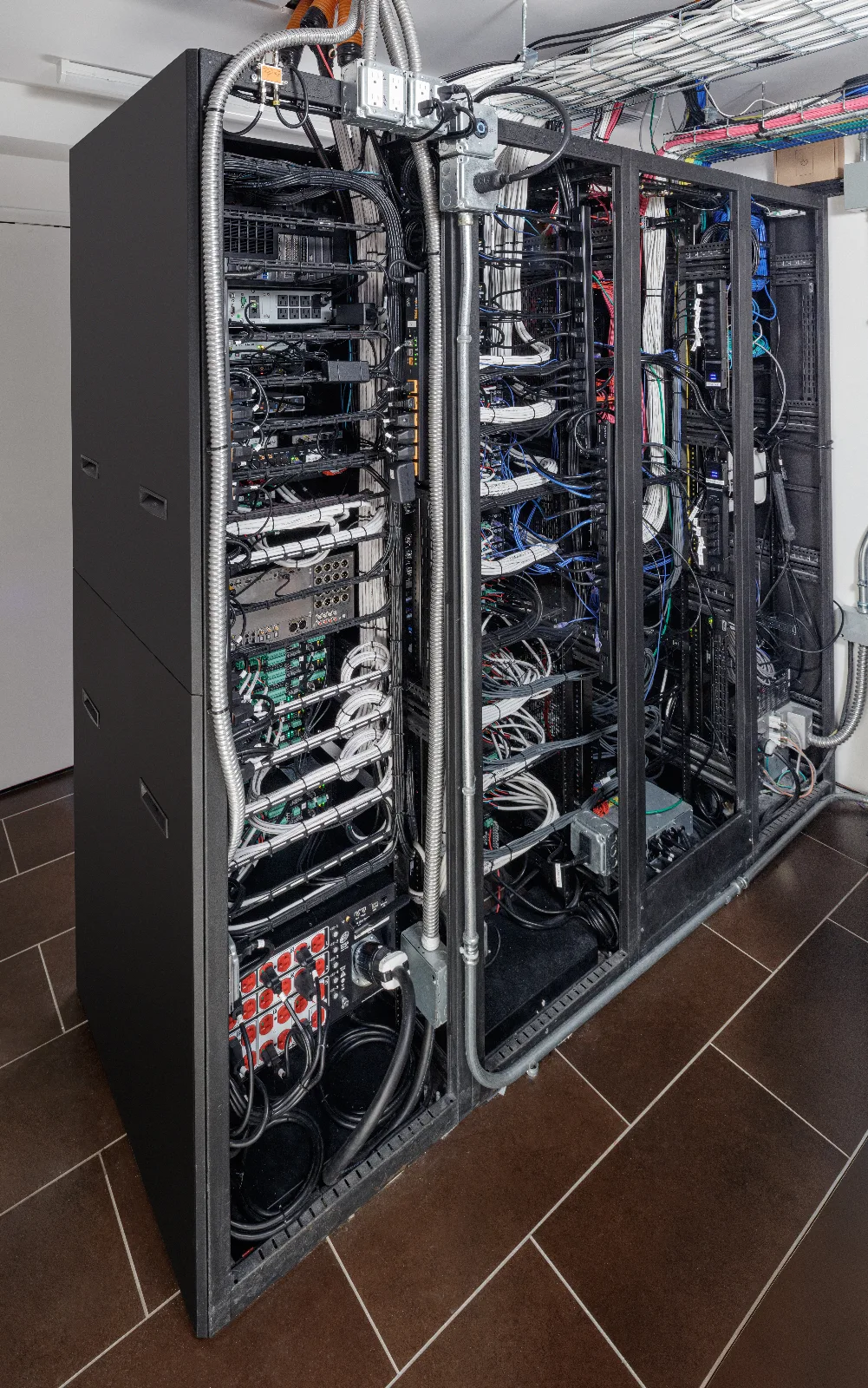 Rear view of multiple black server racks filled with network equipment, servers, and extensive, organized cabling.