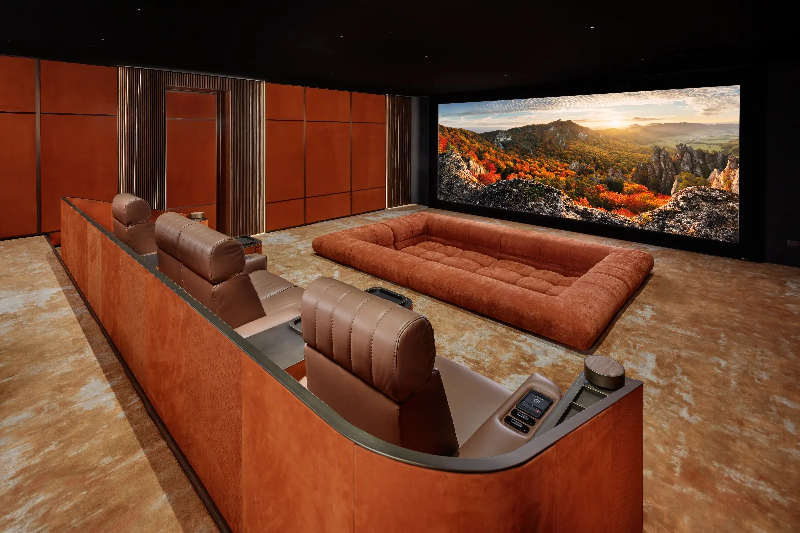 Luxurious home theater with tiered leather seating, a floor cushion, and a large screen displaying an autumn landscape.