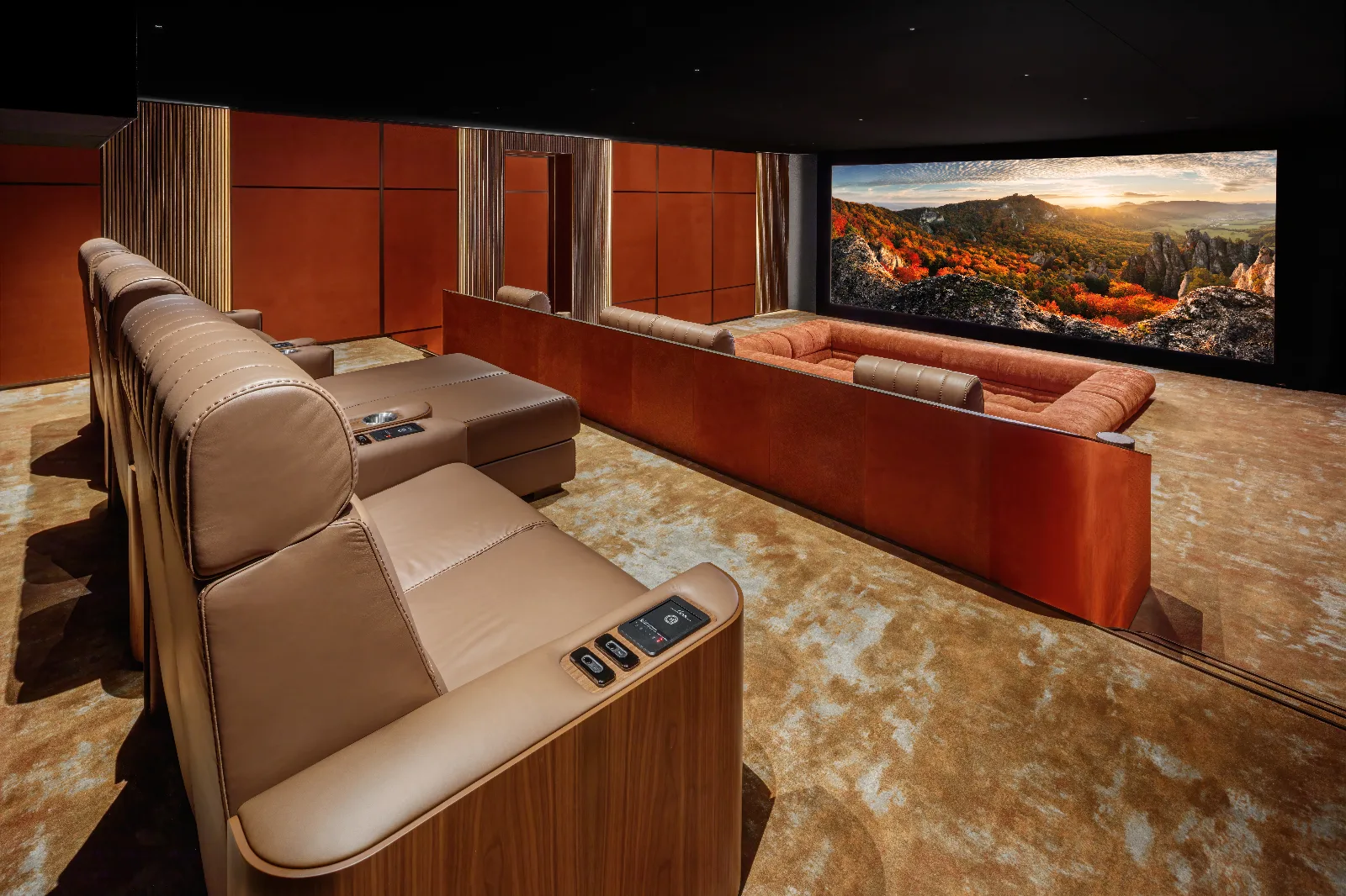 Luxurious home theater with tan leather recliners, an orange sofa, and a large curved screen displaying a colorful landscape.